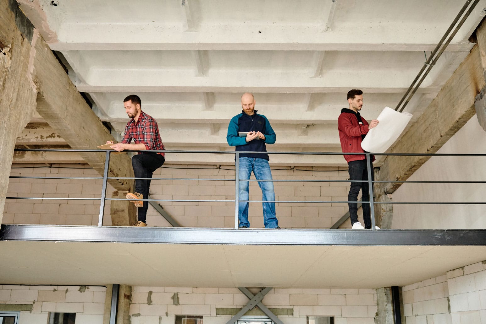 Balcony Inspection young-builder-making-working-notes-while-his-colleagues-using-touchpad-looking-sketch-blueprint-by-railings-unfinished-building